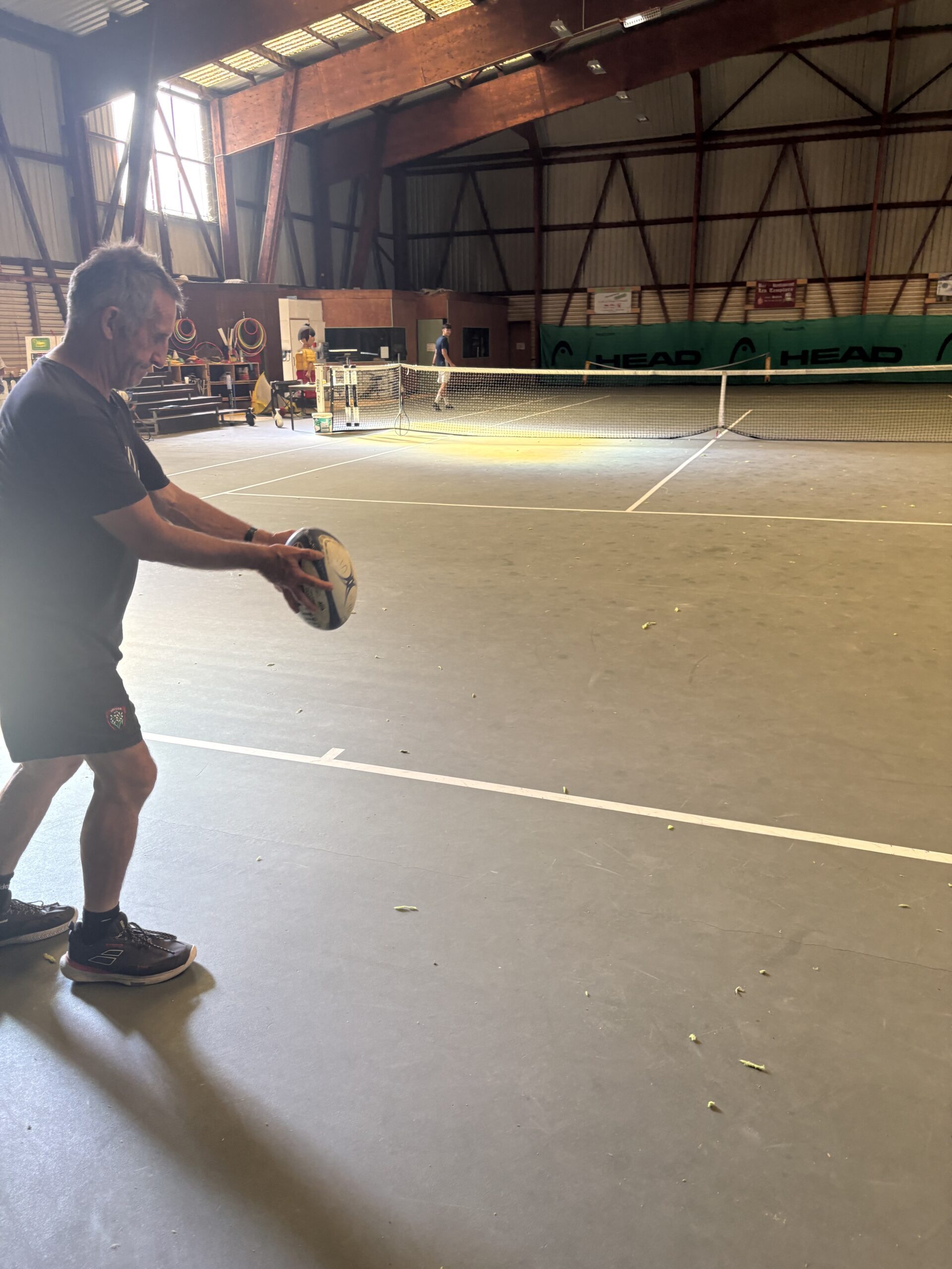 Olivier Miranda s'apprête à engager au pied un ballon de rugby sur un court de tennis couvert à Mauriac