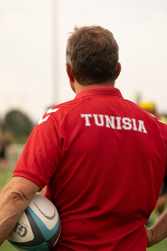 Christophe Hamacek de dos, ballon sous le bras, en polo rouge floqué Tunisia